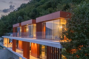 Un immeuble moderne à plusieurs étages, doté de grandes fenêtres en verre, d’un balcon et d’une piscine.