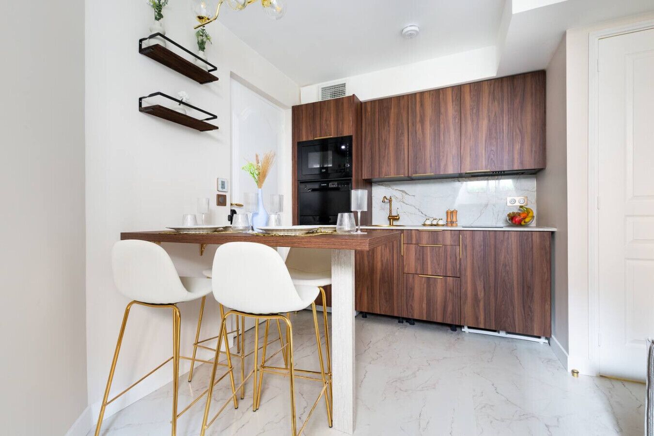 Una cocina moderna con armarios de madera oscura, encimera de mármol y taburetes de bar con marco dorado.