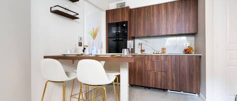 Una cocina moderna con armarios de madera oscura, encimera de mármol y taburetes de bar con marco dorado.