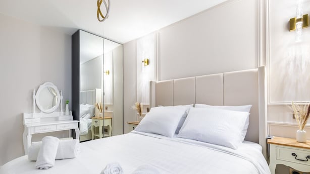 Une chambre d’hôtel avec un grand lit, une coiffeuse avec un miroir et une table de chevet avec une lampe.