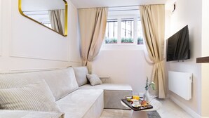 Une pièce moderne et bien éclairée, avec un canapé, une petite table sur laquelle sont disposés des articles pour le petit-déjeuner, un téléviseur et une fenêtre avec des rideaux.