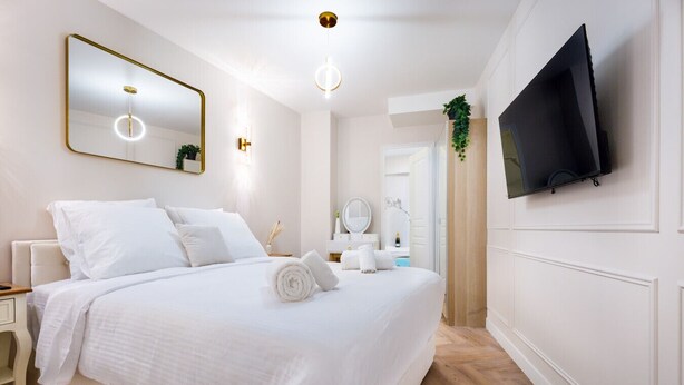 Habitació d'hotel moderna amb un llit gran, una taula de nit, un mirall, un televisor fixat a la paret i una petita planta.