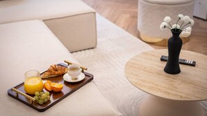 Un plat de petit esmorzar amb suc d'aranja, raïm, un croissant i una tassa de cafè damunt un safata de fusta, col·locat sobre un sofà beix.