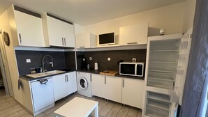 A compact kitchen with white cabinets, a washing machine, a microwave, and a small table. - Studio port Leucate, first line beach (Leucate)
