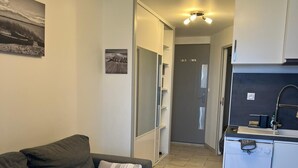 A modern living room with a grey sofa, a small white table, and a kitchen area with a dishwasher. - Studio port Leucate, first line beach (Leucate)