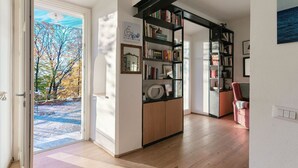 Um quarto com piso de madeira, estante, porta que dá para o exterior e quadro na parede.