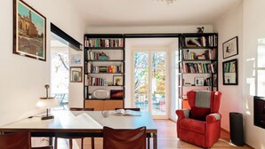 Um quarto com uma mesa de jantar, cadeiras, uma poltrona vermelha, estantes e um candelabro.