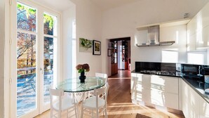 Cozinha moderna com armários brancos, mesa de jantar de vidro e vista por uma porta de vidro.