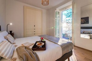 A bedroom with a bed, a bedside table, a lamp, a window with a view, and a door. - Villa Rocawood - MyHomeinComo (Brunate)