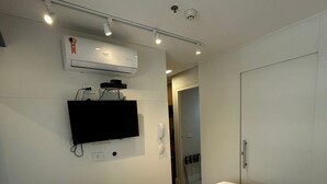 A bedroom with a bed, a mounted TV, an air conditioning unit, and a door leading to another room. - Get a Flat - 604  Ibirapuera (São Paulo)