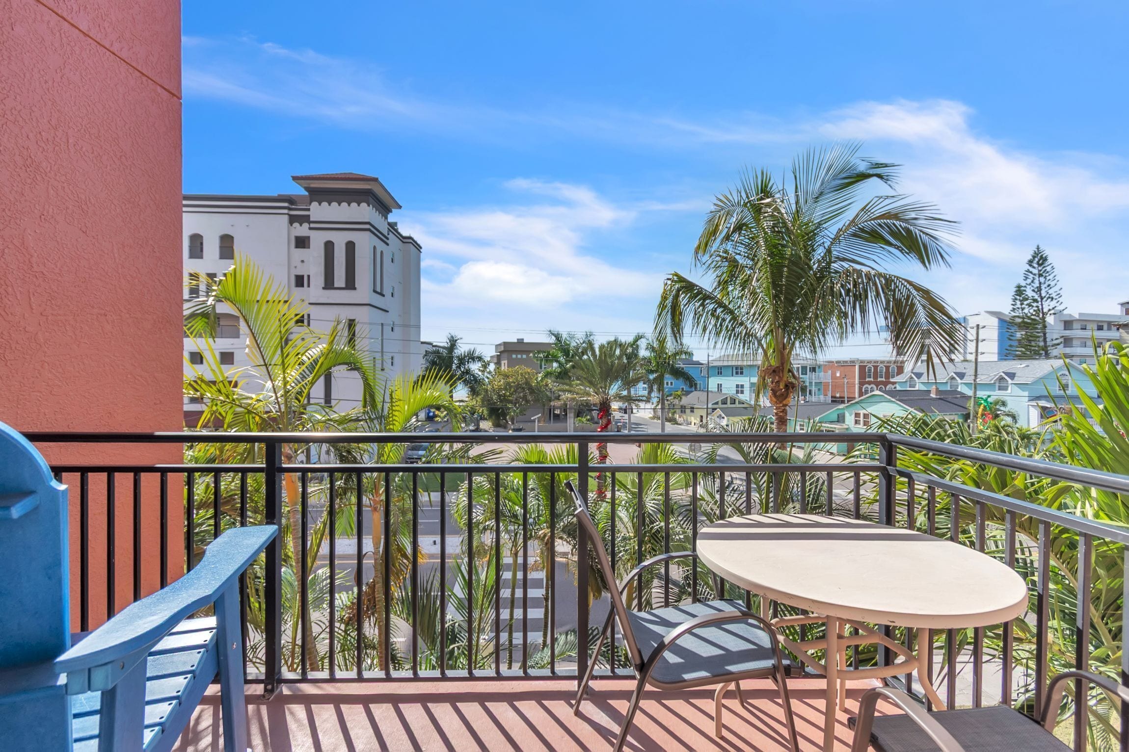 A balcony with a table and chairs, overlooking a street with buildings and palm trees.