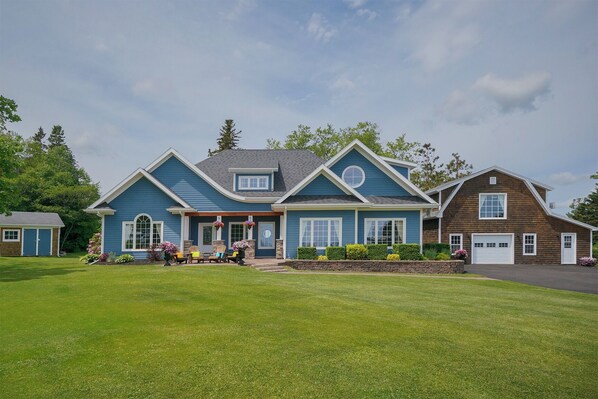 A two-story house with a front porch, a garage, and a well-maintained lawn. - Harbourview Retreat - Waterview Luxury Home Steps from the Inn at Bay Fortune (Rock Barra)