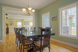 A dining room with a large table, six chairs, a chandelier, and large windows with a view of the outdoors. - Harbourview Retreat - Waterview Luxury Home Steps from the Inn at Bay Fortune (Rock Barra)