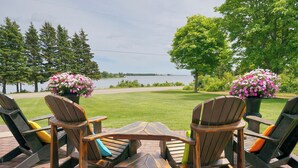 A patio with Adirondack chairs, a wooden table, and flower pots. - Harbourview Retreat - Waterview Luxury Home Steps from the Inn at Bay Fortune (Rock Barra)