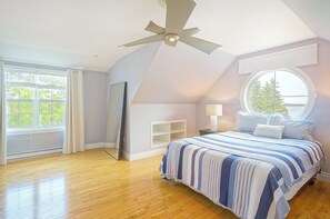 A bedroom with a large bed, a ceiling fan, a window with a view, and a mirror. - Harbourview Retreat - Waterview Luxury Home Steps from the Inn at Bay Fortune (Rock Barra)
