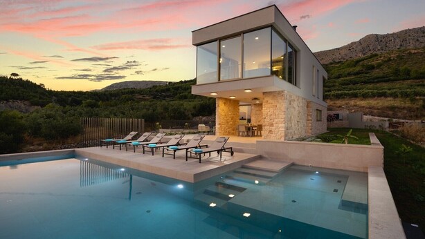 Una casa moderna con piscina, muros de piedra y vistas a las colinas.