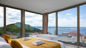 Habitación de hotel moderna con una cama grande, una bañera y vistas a un paisaje costero.