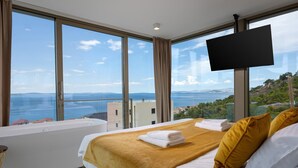 Habitación de hotel con una cama grande, un televisor de pantalla plana y vistas al mar y las colinas.