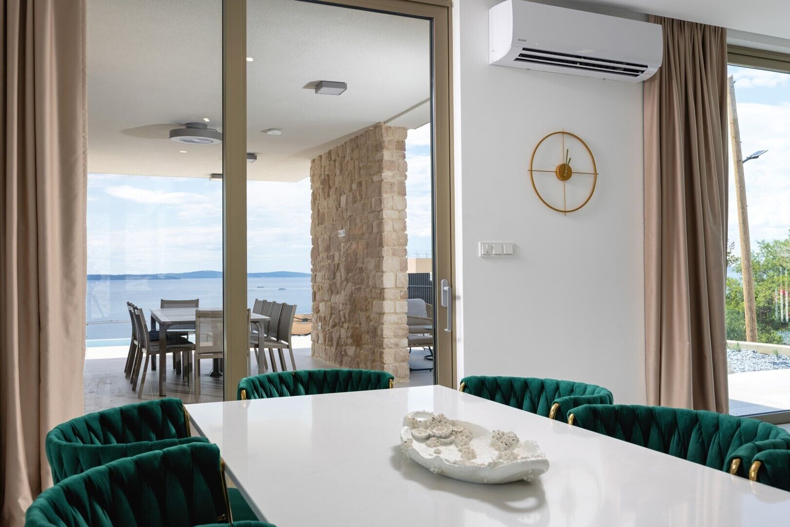 A modern dining area with a white table, green upholstered chairs, and a view of the sea.