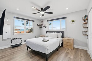 Ein modernes Schlafzimmer mit Bett, Deckenventilator, Nachttisch, Fenster und Blick ins Freie.