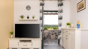 A room with a TV on a cabinet, a clock on the wall, and a view of greenery outside. - Holiday home Rozara by Villas Guide (Primošten)