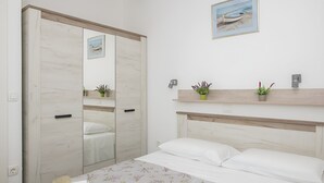 A bedroom with a bed, a wardrobe, a mirror, a shelf with plants, and a picture on the wall. - Holiday home Rozara by Villas Guide (Primošten)
