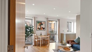 A modern living room with a dining area, a sofa, a table with a candle, and a large window. - Bywell Apartment, Canning Town, London (Greater London)