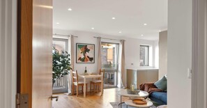 Ein modernes Wohnzimmer mit Essbereich, einer Couch, einem Tisch mit Kerze und einem großen Fenster.