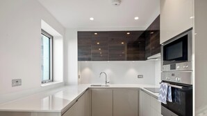 A modern kitchen with a built-in oven, a microwave, and a sink. - Bywell Apartment, Canning Town, London (Greater London)