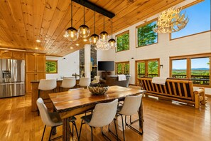 A spacious kitchen with a large island, a dining area with a wooden table and chairs, and a view of the outdoors through large windows.