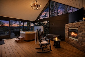 A wooden deck with a hot tub, a fireplace, and a rocking chair.