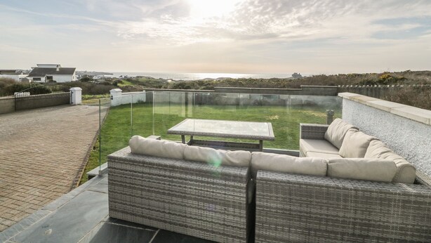 Um terraço no telhado com um sofá de vime e uma mesa, com vista para uma área gramada e o mar.