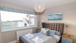 Quarto com uma janela grande, cabeceira estofada, um quadro e um candelabro.