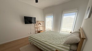 A bedroom with a bed, a TV, a window, and a wooden floor.