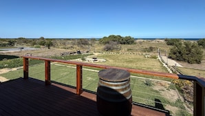 A wooden deck with a railing overlooking a grassy area and a clear view of the ocean.