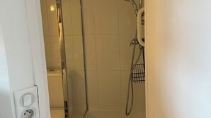 Ein kleiner, abgeschlossener Duschbereich mit Glastür, Handbrause und integriertem Sitzplatz.