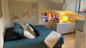 Ein Schlafzimmer mit einem Bett, Kissen, einem Fernseher, einer Lampe und einem kleinen Tisch mit einem Korb.