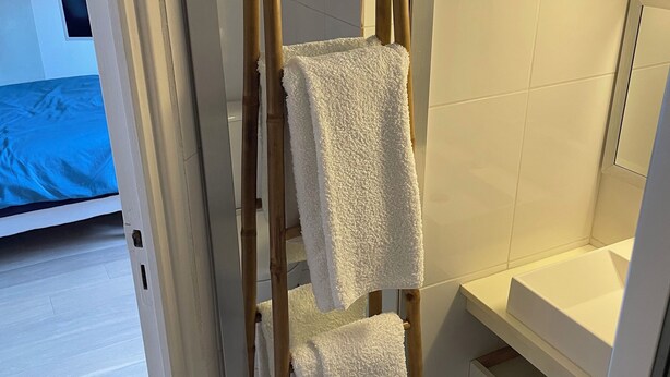 Ein Badezimmer mit einem hölzernen Handtuchhalter, der zwei weiße Handtücher trägt, einer grünen Mülltonne und einer weißen Badewanne.