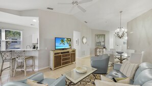 Uma sala de estar ampla, com televisão, área de estar e mesa de jantar.
