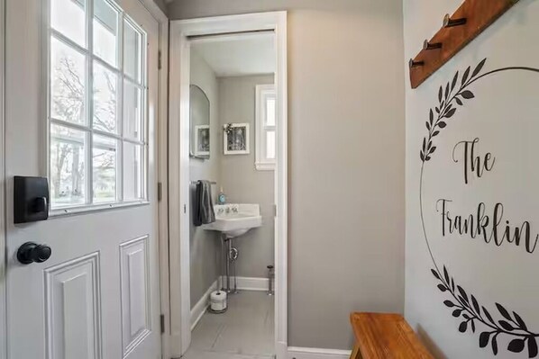 A hallway leading to a bathroom with a white door, a bench, and a wall with the text "The Franklin". - The Franklin Suite- Near Jennings Sports Complex (Lewis Center)