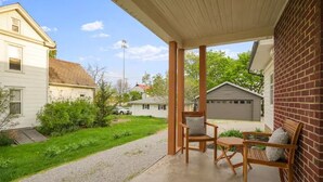 A covered patio area with two wooden chairs and a table, a brick wall, and a view of neighboring houses. - The Franklin Suite- Near Jennings Sports Complex (Lewis Center)