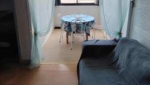 Ein Zimmer mit einem runden Tisch, zwei Stühlen, einem schwarzen Sofa und einem Fenster mit Vorhängen.