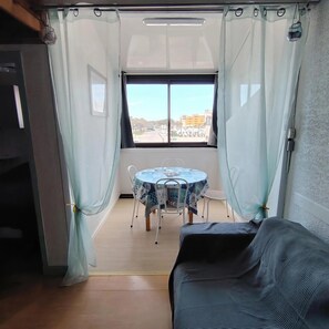 Ein Zimmer mit einem runden Tisch, zwei Stühlen, einem schwarzen Sofa und einem Fenster mit Vorhängen.
