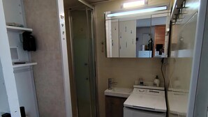 Ein kleines Badezimmer mit Toilette, Duschkabine, Waschbecken mit Spiegel und kleinem Kühlschrank.