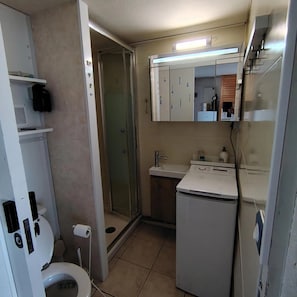 Ein kleines Badezimmer mit Toilette, Duschkabine, Waschbecken mit Spiegel und kleinem Kühlschrank.