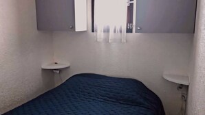 Ein kleines Schlafzimmer mit einem Einzelbett, einem Nachttisch, einem Spiegel und einem Fenster mit Vorhängen.