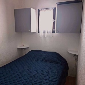 Ein kleines Schlafzimmer mit einem Einzelbett, einem Nachttisch, einem Spiegel und einem Fenster mit Vorhängen.