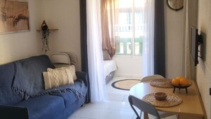 A living room with a blue sofa, a dining table with a bowl of fruit, and a view of a balcony with a bed. - Haven of serenity 100 m from the beach and shops (Le Barcarès)