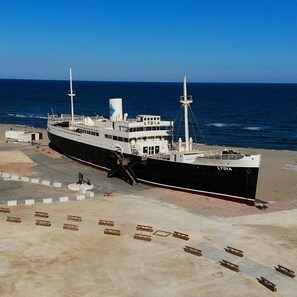 Ein großes Schiff mit dem Namen 'LYDIA' liegt an einem Strand bei strahlendem Himmel vor Anker.
