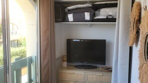 A room with a television on a wooden cabinet, a window with a view of greenery, and a curtain. - Haven of serenity 100 m from the beach and shops (Le Barcarès)